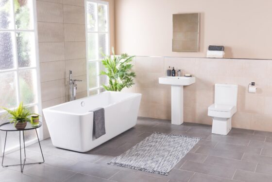 A modern bathroom with a freestanding bathtub, large windows allowing natural light, a green plant on the side, and minimalistic design elements showcasing a blend of style and functionality.