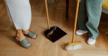 Parent sweeping a light-colored vinyl floor in a children's room with toys